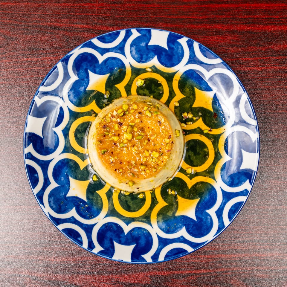 Pistachio-topped orange dessert served in a glass dish on a colorful patterned plate.