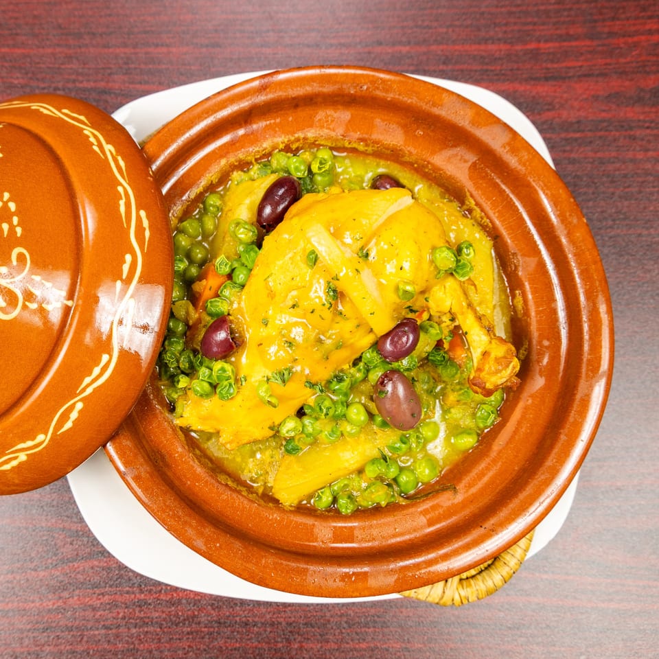 Chicken tagine with green peas, carrots, and olives served in a decorative terracotta dish.