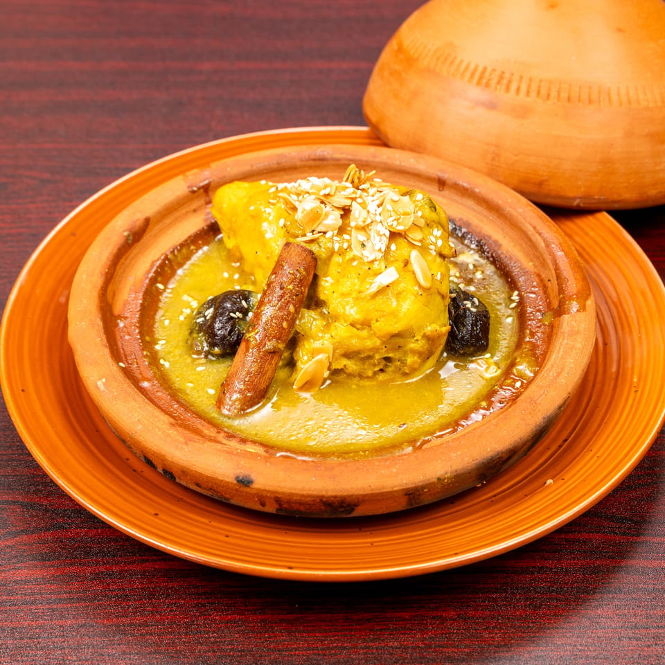 Moroccan tagine with chicken, prunes, almonds, sesame seeds, and cinnamon served in a clay dish.