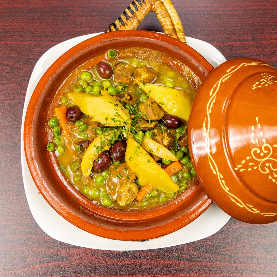 Moroccan tagine with tender meat, peas, potatoes, carrots, and olives in a decorated terracotta dish.