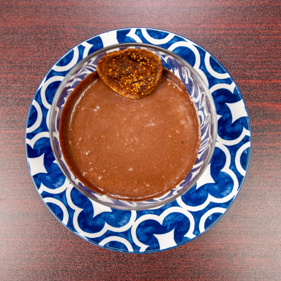 Chocolate dessert topped with a dried fig, served in a glass bowl on a blue-and-white patterned plate.