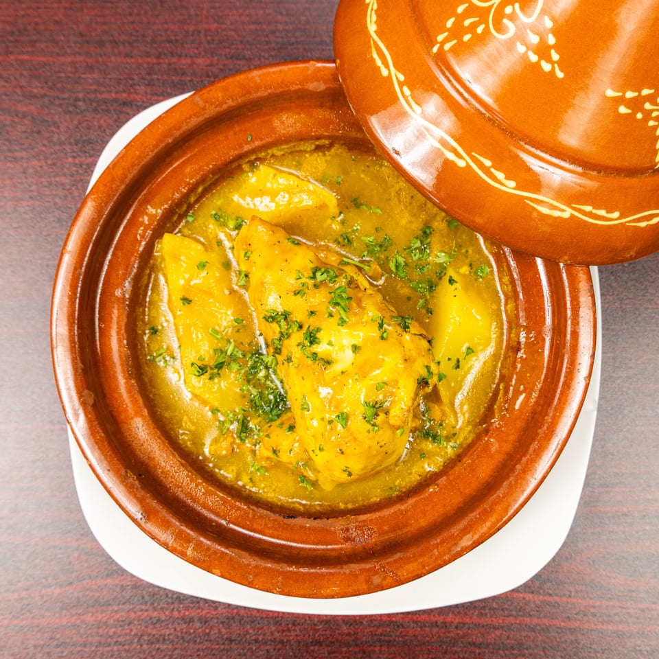 Golden chicken tagine garnished with herbs in a traditional decorated clay dish on a wooden table.