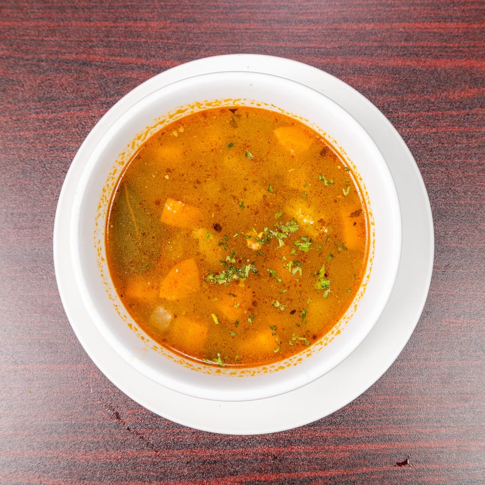 Bowl of orange spiced curry with vegetables and chopped cilantro, served on a white plate atop a patterned tablecloth.