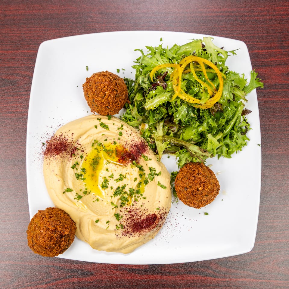 Plate of creamy hummus with falafel, mixed green salad, yellow pepper strips, herbs, and spices.